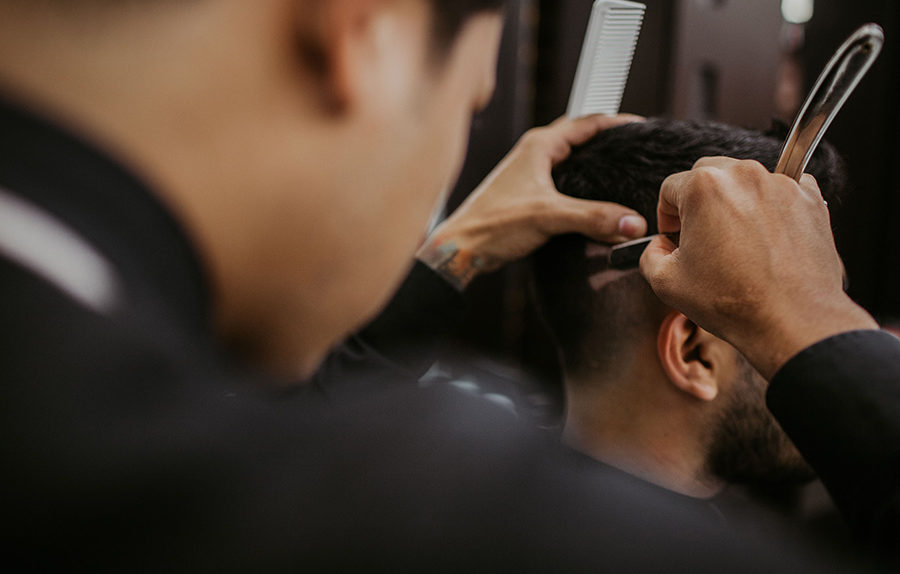 Barber giving man haircut and shaving with blade and comb