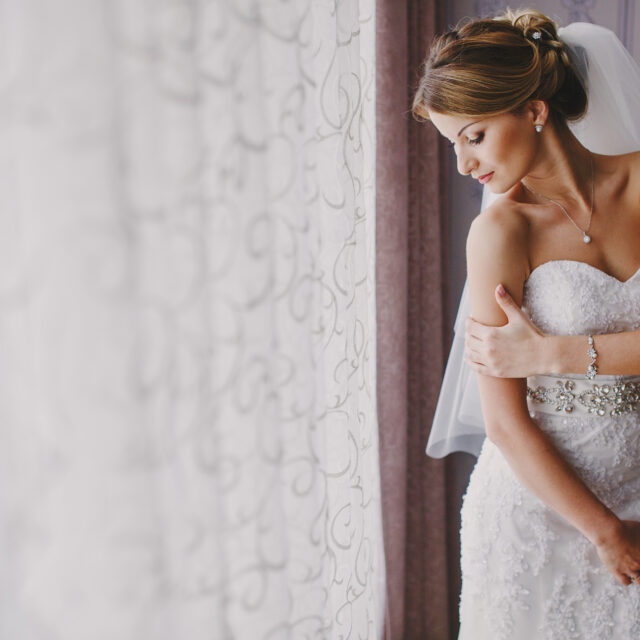 bride-standing-by-window-in-wedding-dress
